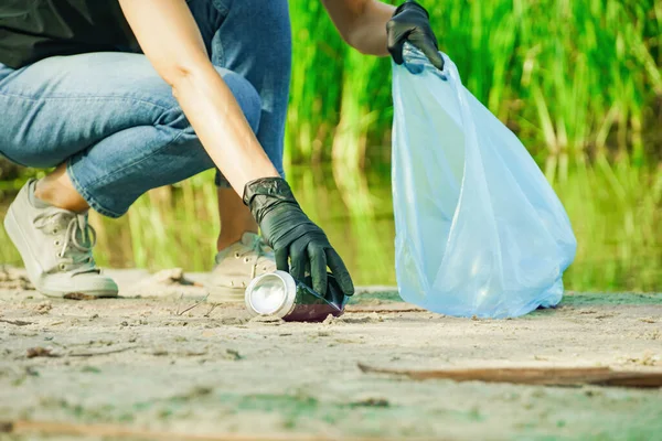 Kadın çöp torbasında çöp kutusu topluyor. Doğadaki sahil nehrinde çöp toplama