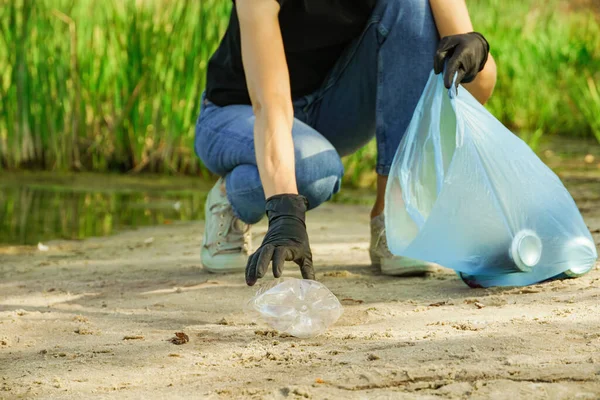 Gönüllü kadın çöp torbasına plastik bir şişe koydu. Orman doğasında çöp toplama.