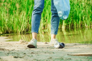 Gönüllü kadın çöp torbasına alüminyum kutu koymuş. Orman doğasında çöp toplama.