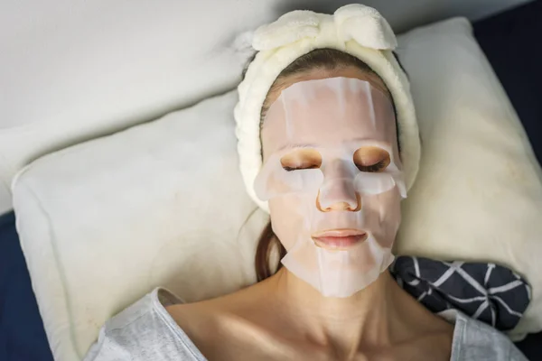 Woman with a cloth moisturizing mask on her face lie in bedroom