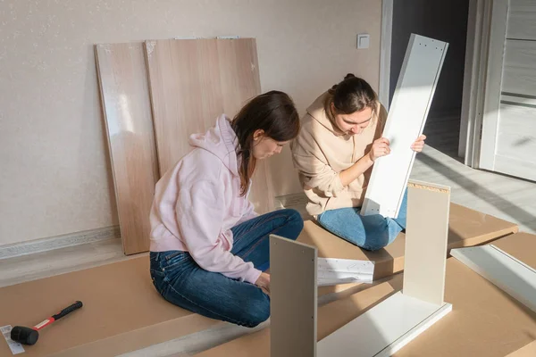 Millennial women reading instructions to DIY and self assemble furniture. Moving in new house. Self-assembly furniture concept
