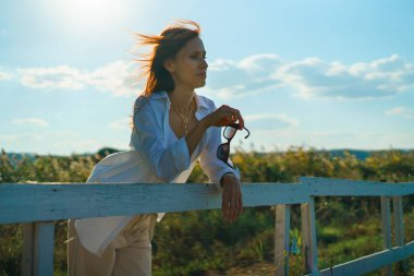 Çiftlikte dinlenen ve gün batımında tarla manzarasının tadını çıkaran bir kadın.