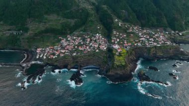 Madeira Adası 'ndaki Seixal' da okyanusun üzerinde kümelenmiş kıyı evleri var. Atlantik kıyı şeridi ve bulutlu havada dağlık zemin