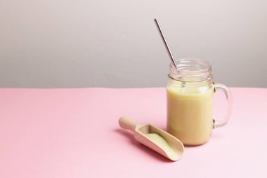 Geleneksel Japon yeşil çayı, cam kavanozda latte ve pembe arka planda saman içmek..