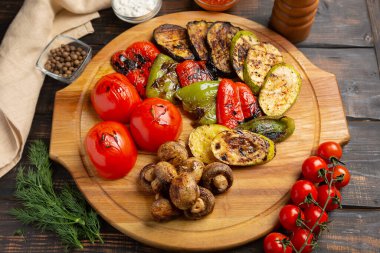 Mantarlı ızgara sebzeler, yuvarlak kesim tahtası, koyu ahşap arka plan.