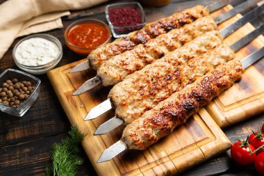 Kebap metal şiş üzerinde kıyma, sebze ve ahşap arka planda sos.