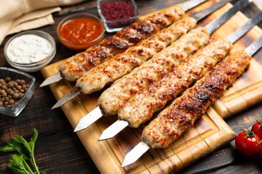 Kebap metal şiş üzerinde kıyma, sebze ve ahşap arka planda sos.