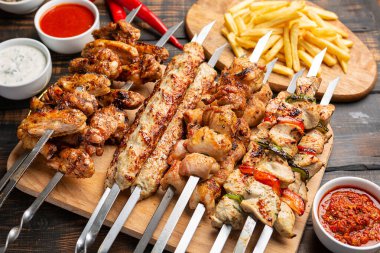 Koyu ahşap arka planda patates kızartması ve soslu çeşitli tavuk kebabı.