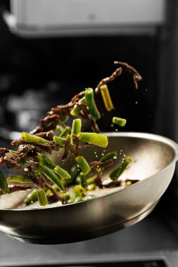 The chef is frying meat and pea pods in a wok, tossing them into the air