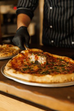 Pizzayı yuvarlak bir bıçakla parçalara ayır. Önlüklü bir adam sıcak Napoli pizzası keser.