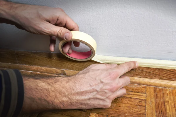 Worker protecting batten moulding with masking tape before paint — Stock Photo, Image