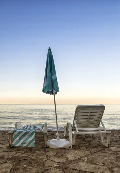 Sillas y sombrilla en una playa al amanecer — Foto de Stock