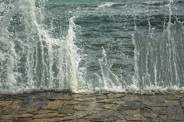 Wellen brechen an einem steinigen Strand auf und bilden eine Gischt. — Stockfoto