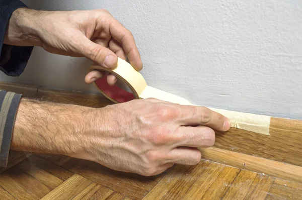 Arbeiter schützt Leisten vor Farbe mit Klebeband — Stockfoto