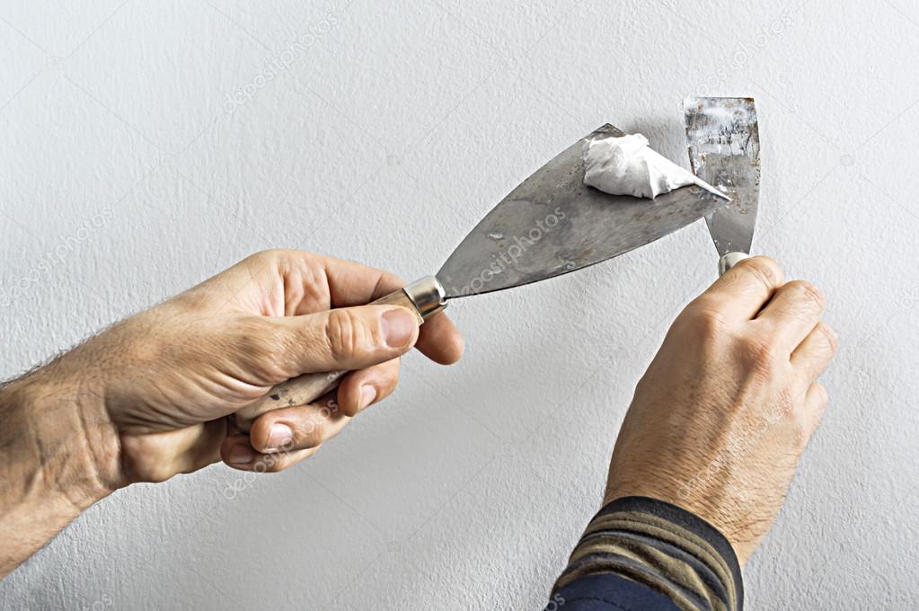 Worker with putty knife working on apartment wall filling