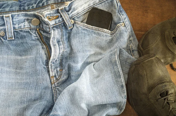 Detail modré džíny s černými botami na dřevěné pozadí — Stock fotografie