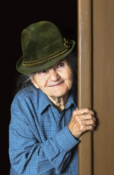 Donna anziana con il cappello che dà una occhiata attraverso porta a casa — Stockfoto