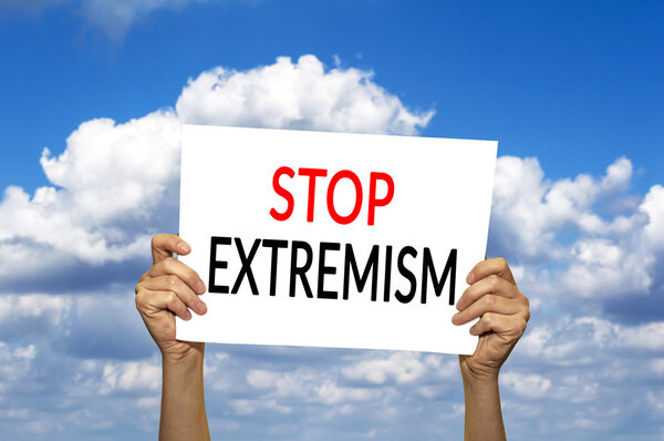 STOP EXTREMISM card in hand against blue sky with clouds. 