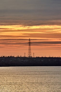 Denizde bir adadaki elektrik hatları sarı-turuncu renkli günbatımının arka planına karşı.