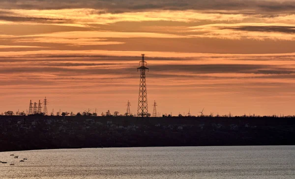Denizde bir adadaki elektrik hatları sarı-turuncu renkli günbatımının arka planına karşı.