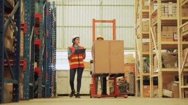 İşçiler büyük bir depoda malları düzenlemek için yük arabalarını sürüklüyorlar..