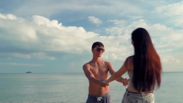 若い家族 カップルの男性と女性が手を握ってアクティブに回転します 海や海を背景に手を取り合って笑っています 夏のテーマ — ストック動画