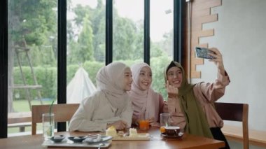 Bir restoranda yemek yiyen bir grup Müslüman kız sosyal medyada göstermek için cep telefonlarını selfie çekmek için kullanıyor..