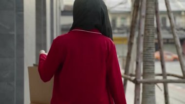 Yavaş çekim video vinci, genç Müslüman bir kadının alışveriş yaptıktan sonra sokakta bir alışveriş çantası taşımasını takip ediyor.