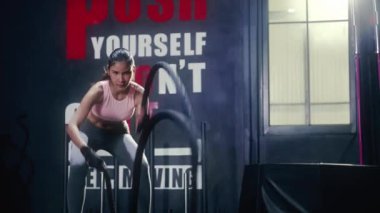 Güzel Asyalı atlet, spor salonundaki kol kaslarını güçlendirmek için halat sallıyor, koyu renk tonda..