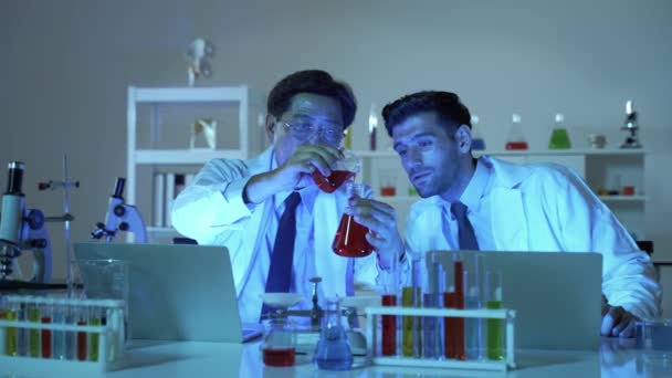 在一个科学实验室里 两名科学家正在把材料倒入试管 并记录结果 他们工作得很匆忙 以便迅速把结果记下来 — 图库视频影像
