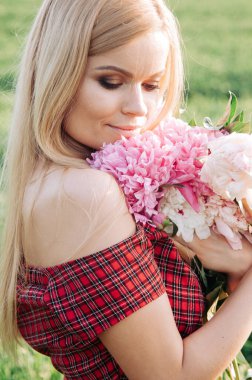 Bahçede şakayıkların yanında poz veren uzun kıvırcık saçlı güzel bir genç kadın. Parfüm reklamı konsepti.