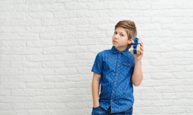 Arka planda neşeli bir kutuyla gülümseyen çocuk. Sevgililer Günü konsepti. Mutlu sarı saçlı ergen, elinde bir hediye beyaz bir arka planda.