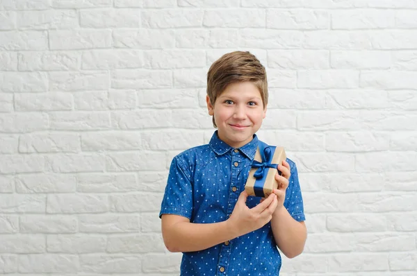 Arka planda neşeli bir kutuyla gülümseyen çocuk. Sevgililer Günü konsepti. Mutlu sarı saçlı ergen, elinde bir hediye beyaz bir arka planda.