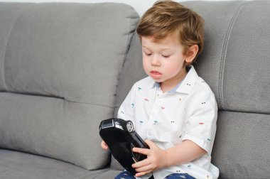 Evde kızıl saçlı küçük bir çocuk, kanepede oynuyor..