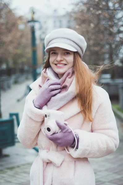 Güneşli bir hayat tarzı portresi, sokakta poz veren, elinde retro film kamerası olan, gülen güzel, neşeli, kızıl saçlı bir kız..