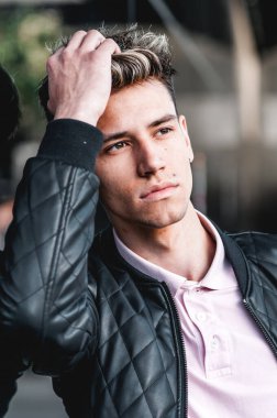 Moda mankeni genç bir adam, günlük kıyafetlerle kentsel arka planda kameraya bakıyor. Sokaklarda modern saç kesimi olan bir adam..