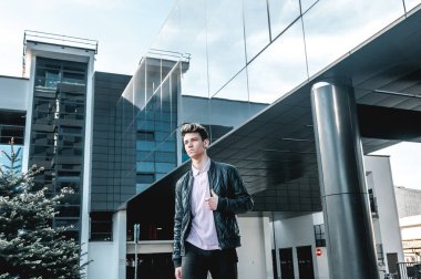 Sıcak bir yaz gününde modern bir binanın yakınındaki bir şehirde şık tişörtlü genç yakışıklı bir adam duruyor. Yürüyüş için şık bir adam.. 