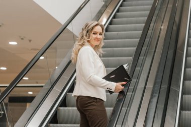 Modern Şehir 'de yürüyen merdiven kullanan sarışın iş kadını. İş kadını yürüyen merdivenden yukarı çıkıyor.