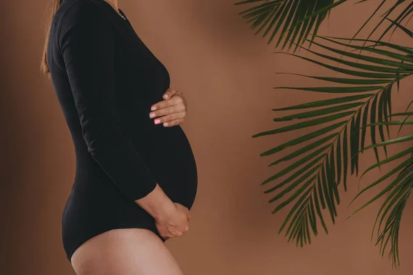 Femme enceinte tient son ventre avec ses mains sur un fond de studio. — Photo