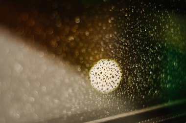 Su, bulanık bokeh arkaplanlı şeffaf cam bir yüzeye düşer.