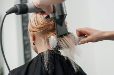 Güzellik salonundaki usta müşterinin saçını kurutuyor..