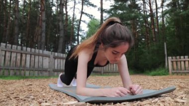 Siyah elbiseli kadın doğada çalışıyor ve spor paspası üzerinde kalas yapıyor. Kapat.