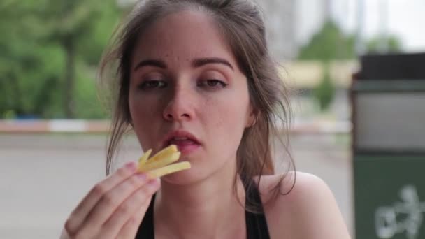 Mujer hambrienta come un montón de papas fritas después del entrenamiento en la calle. De cerca. — Vídeos de Stock