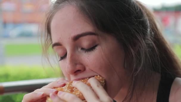 Hongerige vrouw kauwt smakelijk een hamburger na het sporten op straat. Sluiten. — Stockvideo