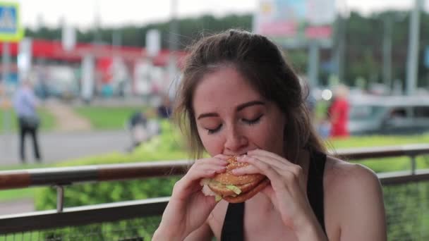 Πεινασμένη γυναίκα μασάει ορεκτικά ένα burger μετά την προπόνηση στο δρόμο — Αρχείο Βίντεο