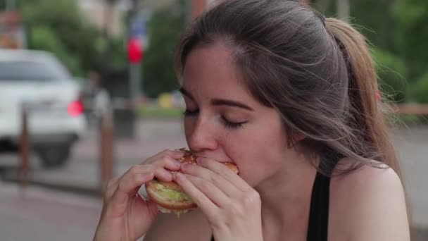 Hongerige vrouw kauwt smakelijk een hamburger na het sporten op straat. Sluiten. — Stockvideo
