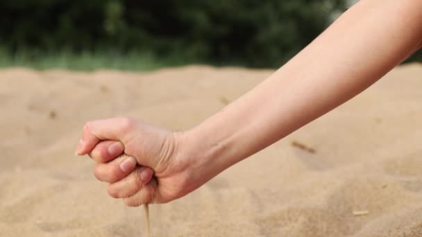 Arena en la mano de la mujer está fluyendo a través de los dedos al suelo en la playa — Vídeo de stock