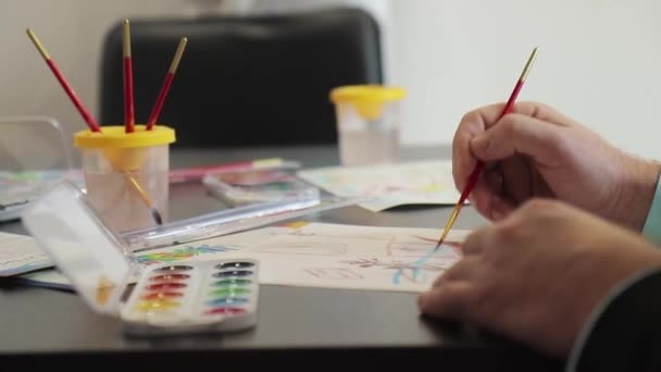 Homem mãos pintar com uma escova em papel com aquarelas na mesa — Vídeo de Stock