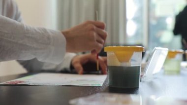 Erkek eli kağıt üzerinde fırçayla resim yapar ve masada suluboya boya yapar.