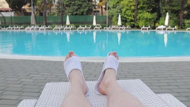 Чоловічі ноги в тапочках біля басейну на сонячному ліжку біля готелю — стокове відео